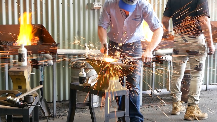 Sparks fly from anvil as man hits molten metal with a hammer.