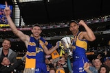 Luke Shuey and Dom Sheed stand on the fence celebrating with the AFL premiership trophy at the MCG.