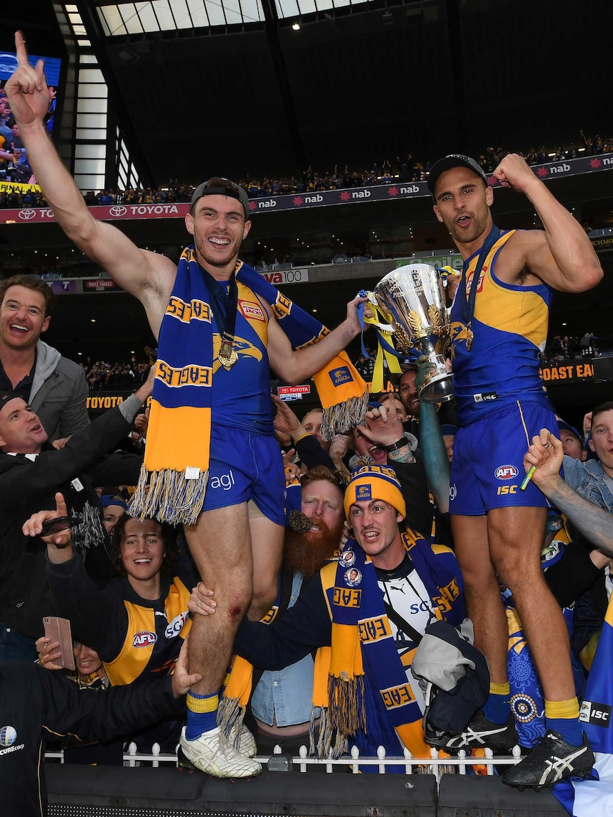 Luke Shuey and Dom Sheed stand on the fence celebrating with the AFL premiership trophy at the MCG.