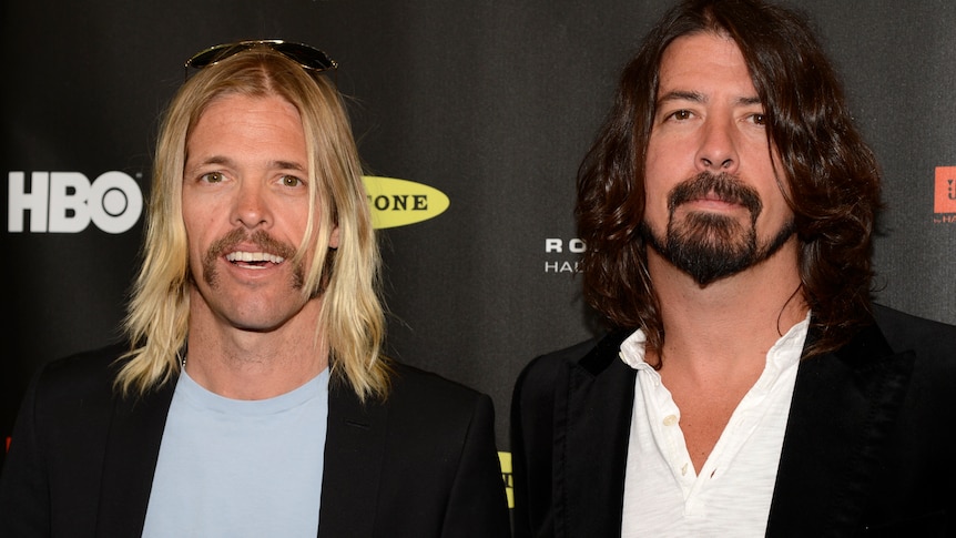 Taylor Hawkins and Dave Grohl standing next to each other and looking at the camera in front of a black background