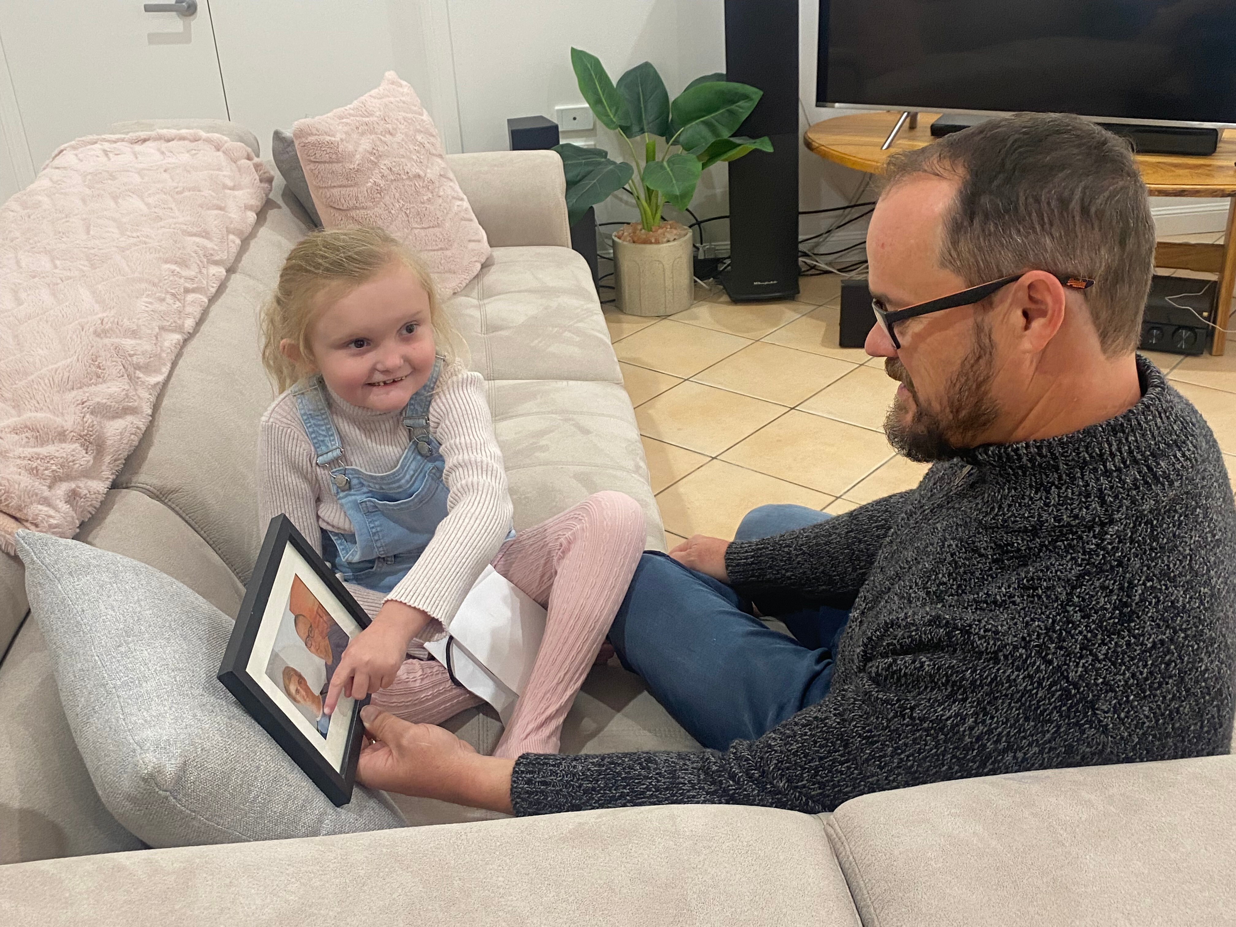 Harper and Shane sitting on a couch with the photo. 