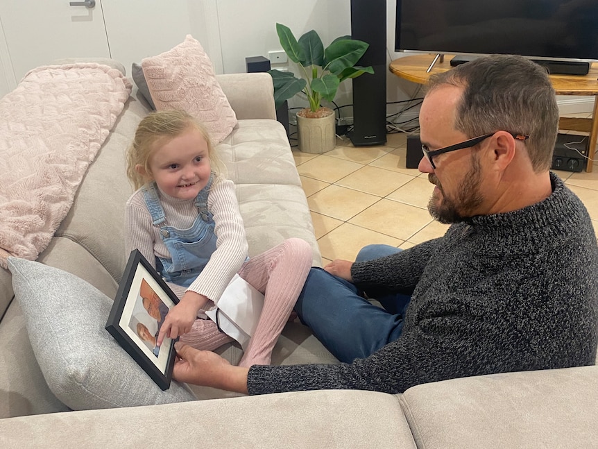 Harper and Shane sitting on a couch with the photo. 