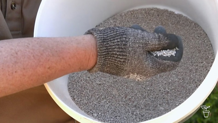 Gloved hand scooping granulated clay from a white bucket.