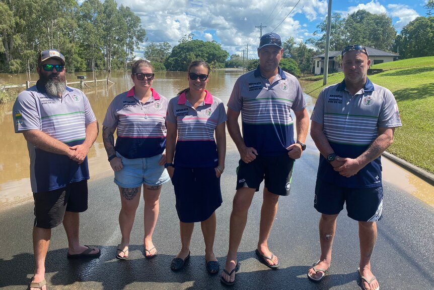 The brothers rugby league board standing in front of a flooded road.