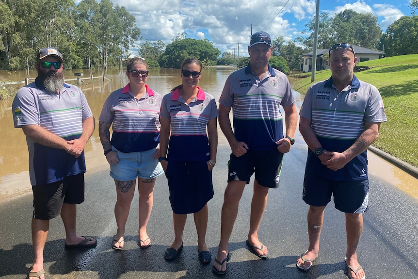 The brothers rugby league board standing in front of a flooded road.