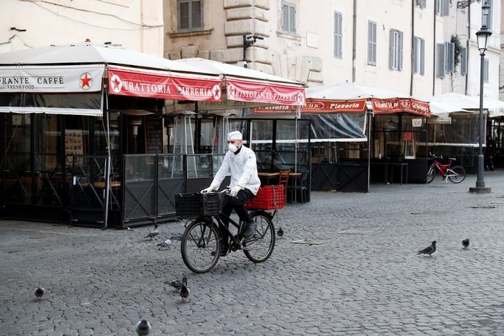 A delivery man wearing a protective face mask rides his bike past a deserted restaurant strip in Rome, Italy.
