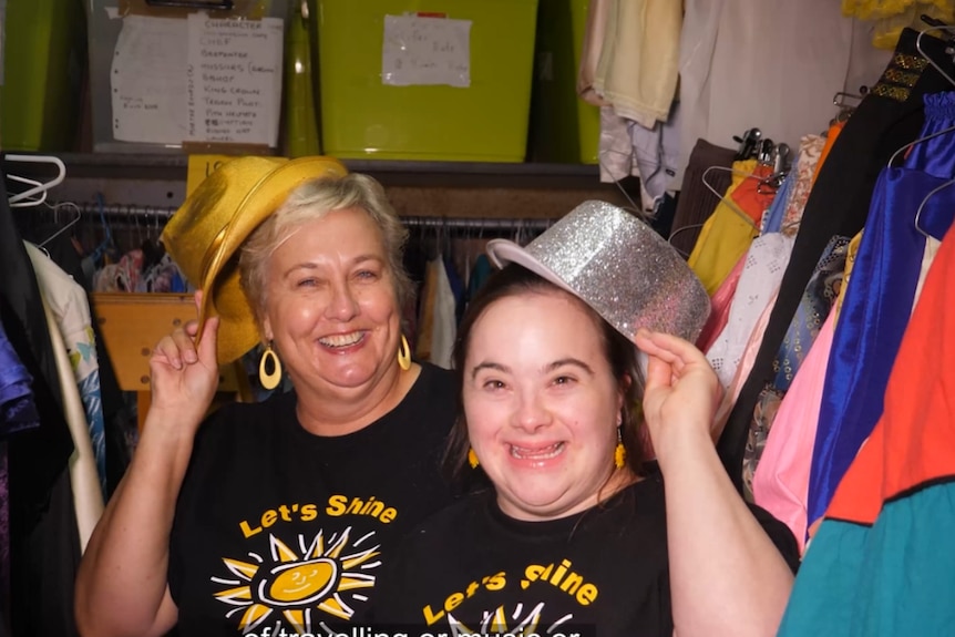 Two smiling ladies hold up sparkly bowler hats and look at the camera.