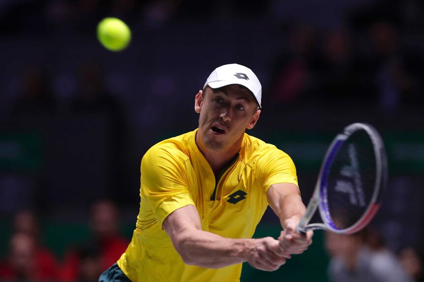 A tennis player grimaces as he gets ready to hit a two-handed backhand.