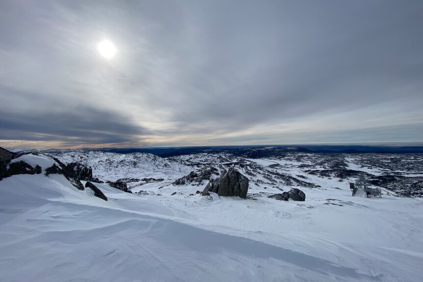 Snowy Mountains in NSW of snow on ground and rocks overlooking horizon with clouds in sky