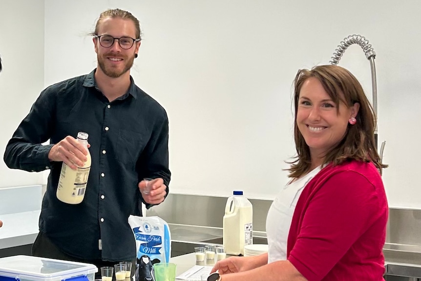 A man and woman stand in a lab holding bottles of milk. 