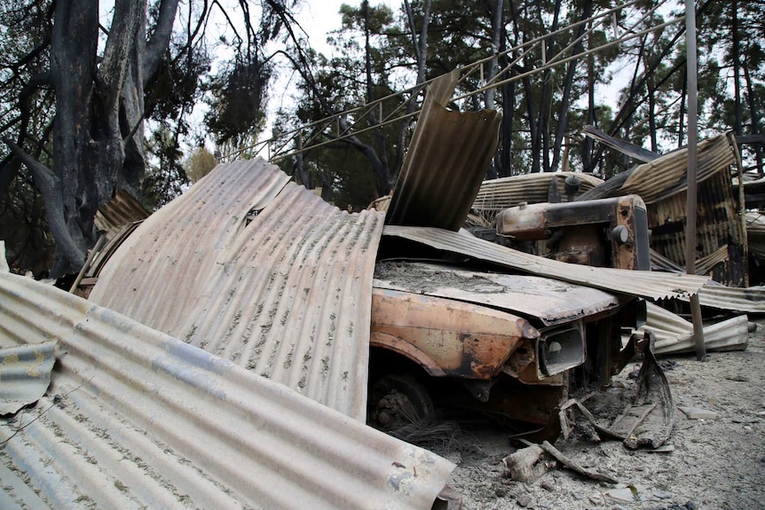 A burnt out car is partially covered in corrugated iron at a property destroyed by fire.