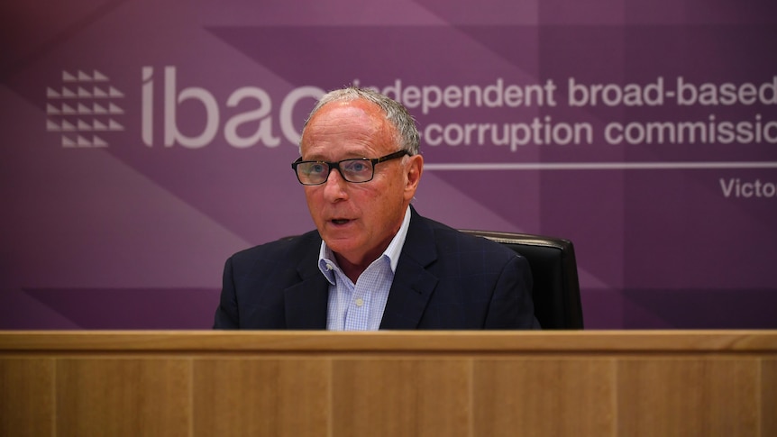A man sits behind a desk, in front of a purple IBAC sign.