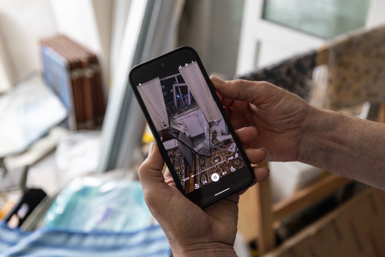 A smartphone screen, with a picture of a badly damaged home visible on it.