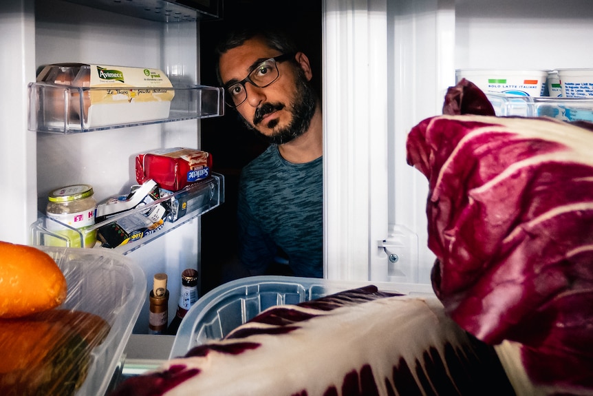 a man looking inside a refrigerator that is full of food