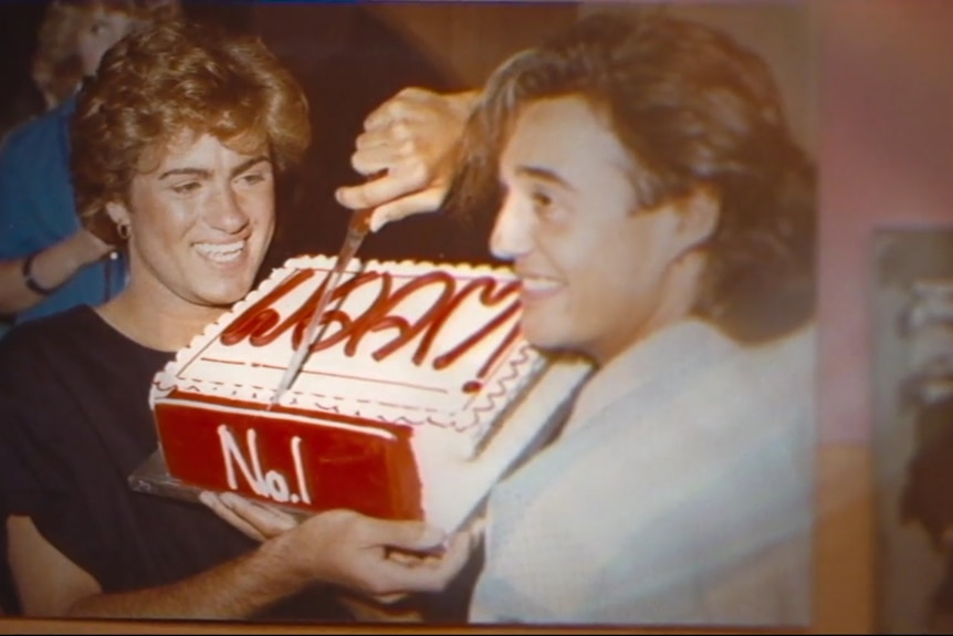 Two men in the 80s holding a big red and white cake