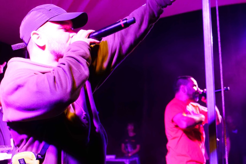 Hip hop artists on stage calling to crowd in purple light.