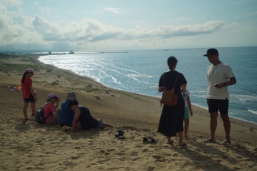 A group of Japanese tourists relax on a beach.