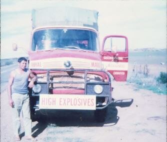 A man leaning on a truck with a high explosives sign on the front