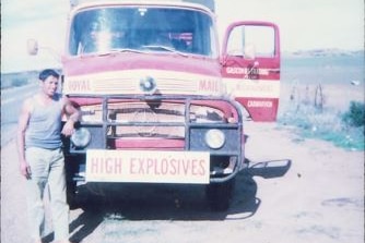 A man leaning on a truck with a high explosives sign on the front