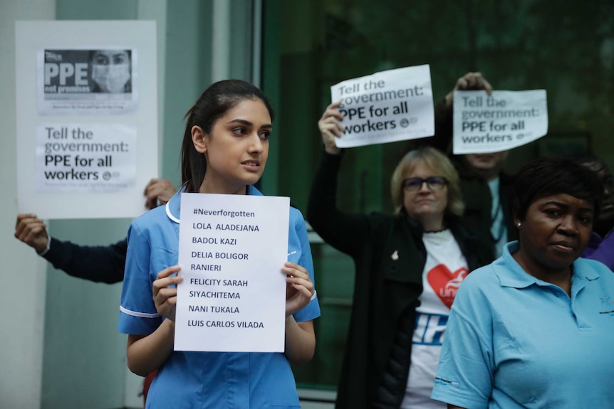 A nurse holds a sign with a list of co-workers who died from coronavirus.