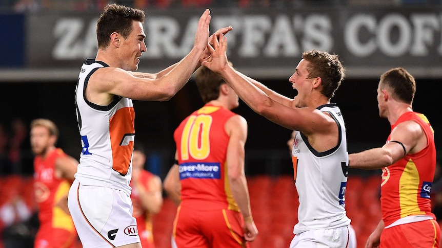 Two AFL players celebrate a goal with a double high five as their dejected opponents walk away.