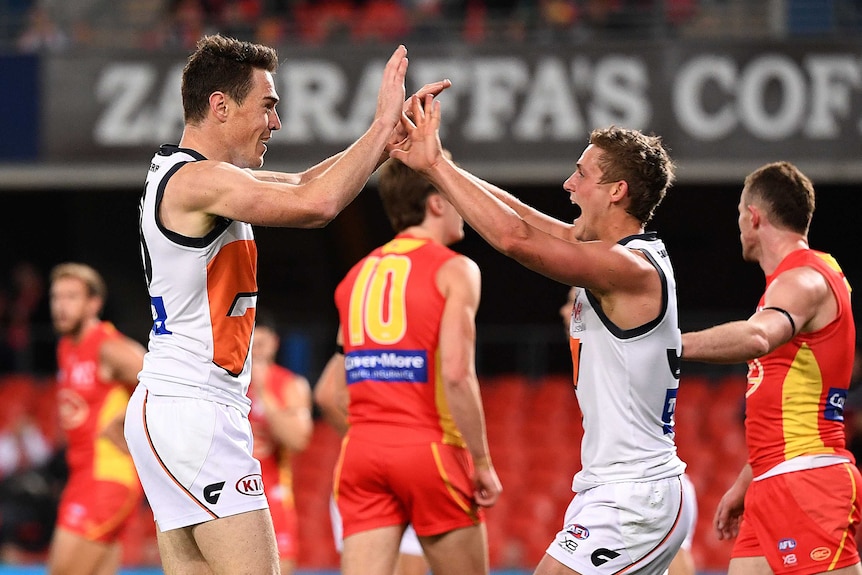 Two AFL players celebrate a goal with a double high five as their dejected opponents walk away.