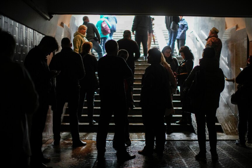 A group of men, women and children are silhouetted against the entrance to a large staircase.