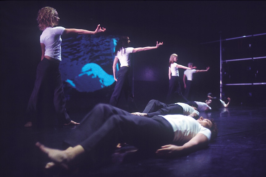 Dancing in white shirt either standing or lying on a black stage