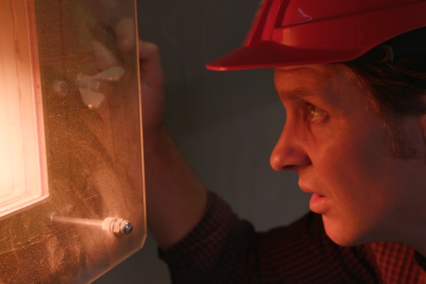 Close view of Craig Reucassel's face cast in the glow of light shining through the window of a waste incineration chamber