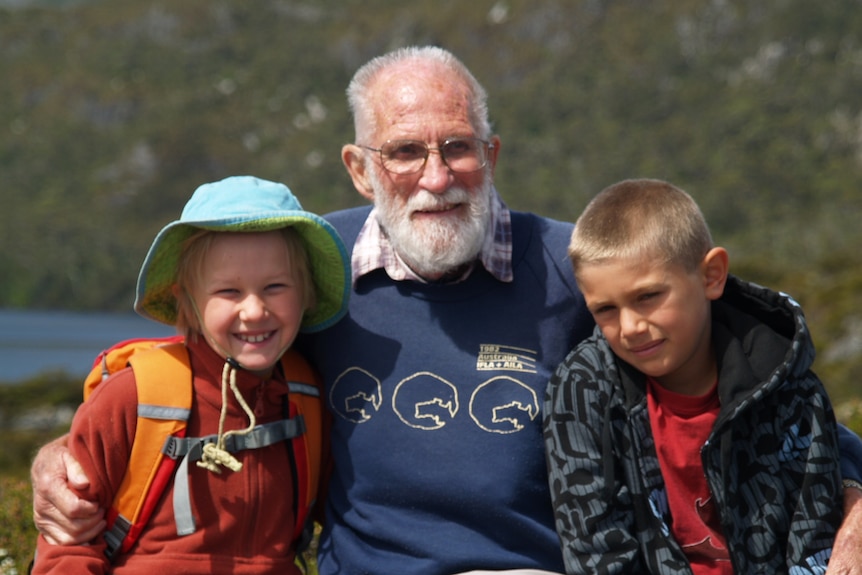 An elderly man sits with two young children