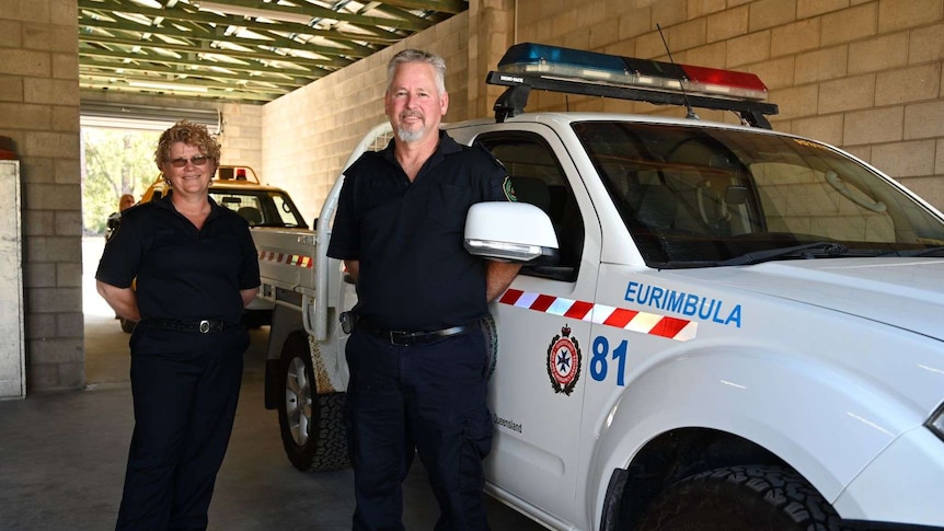 A curly haired woman and a grey haired man stand smiling in front of Rural Fire Service vehicle.