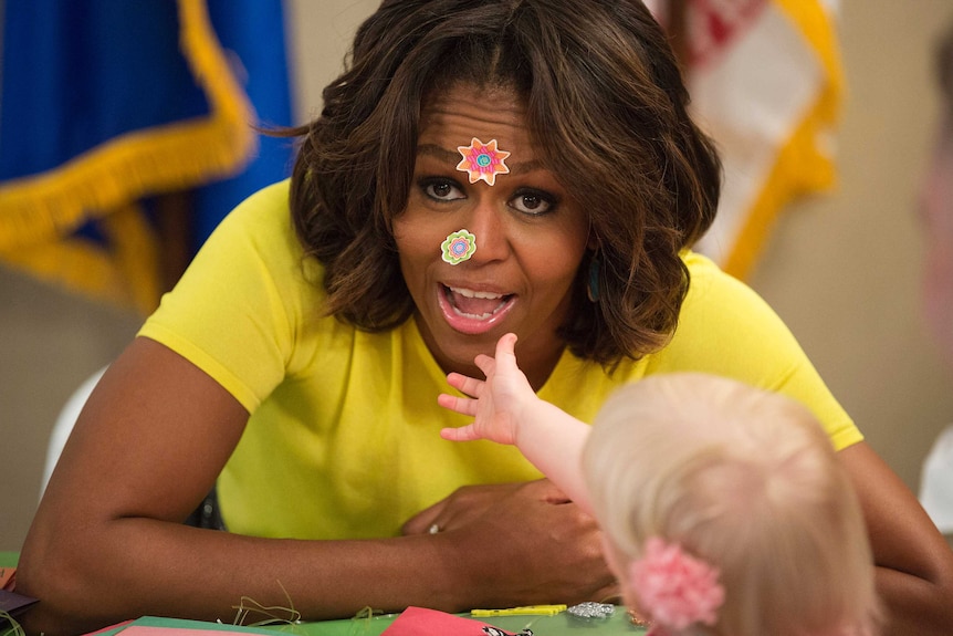 Michelle Obama has stickers put on her face by 20-month-old Lily Oppelt during a visit with children at the Fisher House at Walter Reed National Military Medical Center in Bethesda, Maryland