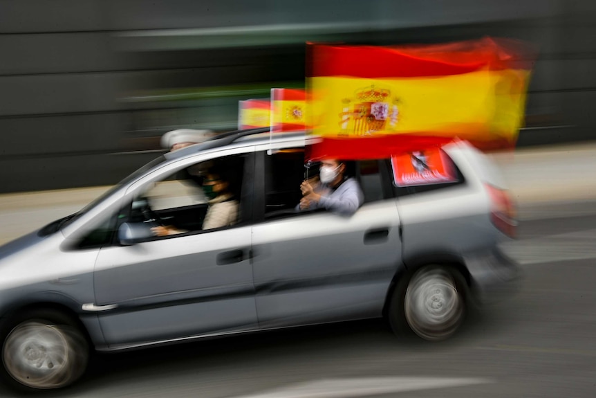 Un manifestante conduce un coche mientras iza la bandera española desde la ventana