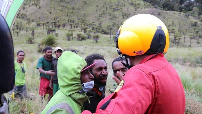 A pilot wearing a helmet talks to a group of people on a mountain.