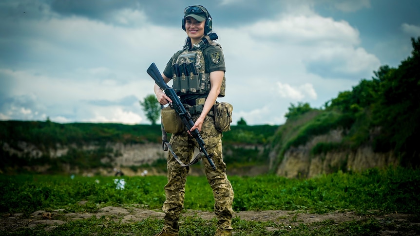 A young female soldier smiles while holding a rifle 