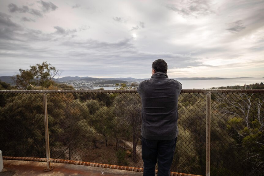 A man looks over a fence towards the ocean.