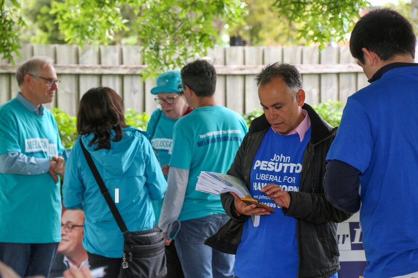 John Pesutto in a blue t-shirt looks a papers standing in front of teal volunteers.