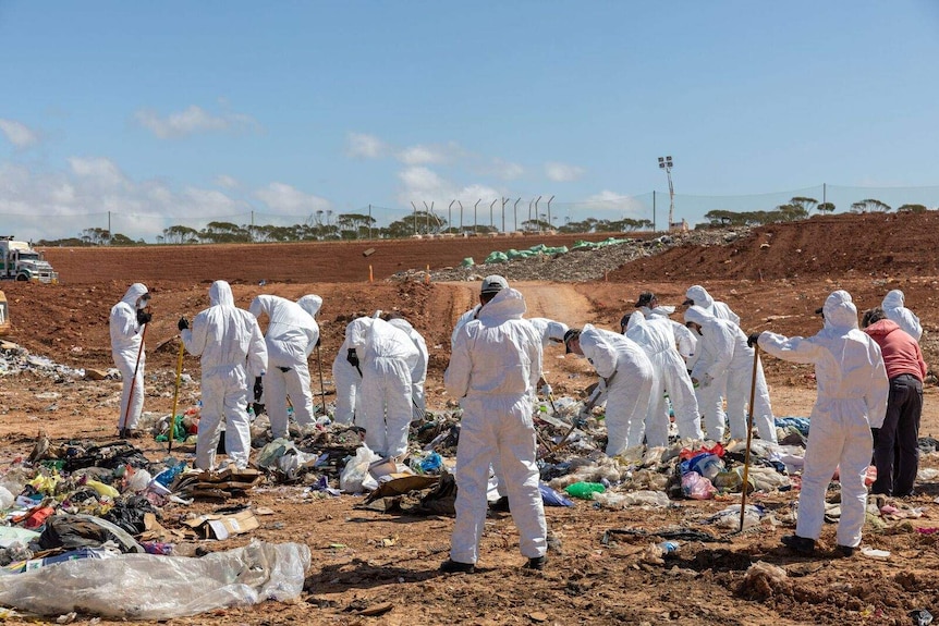 Two police officers scour a rubbish dump.