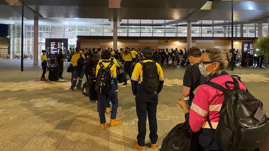 A line of mine workers in high-vis clothing awaiting their rapid antigen testing before boarding their flight to the Pilbara