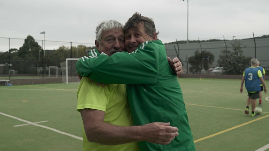 Two older men hug at a walking football game.