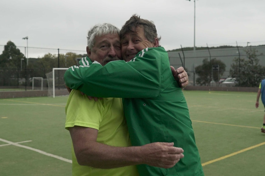 Two older men hug at a walking football game.