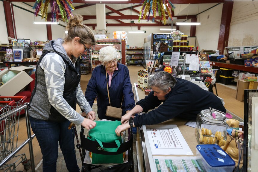 Two staff members  in a country store helping out an elderly customer