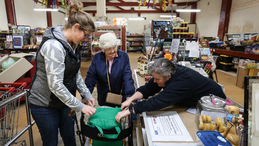 Two staff members  in a country store helping out an elderly customer