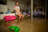 A girl sits on the edge of a sofa in a bedroom filled with floodwater.
