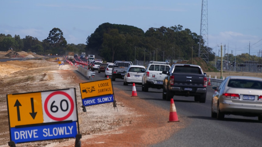 Roadwork signs telling drivers to slow down as a long line of cars navigate through traffic cones.