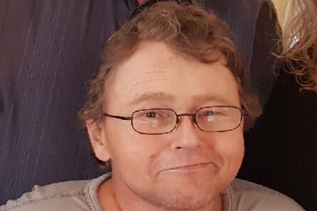 A man with curly blonde hair and glasses smiles at the camera.