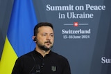 Volodymyr Zelenskyy looking to the right in front of a Ukraine flag and a sign that reads Summit on Peace in Ukraine. 