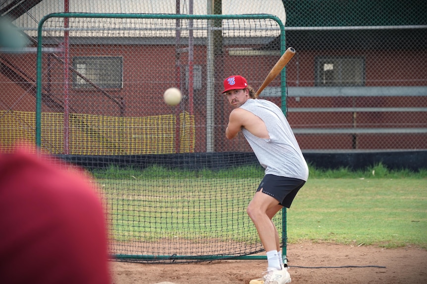 A man holding a baseball bat prepares to hit a baseball travelling towards him