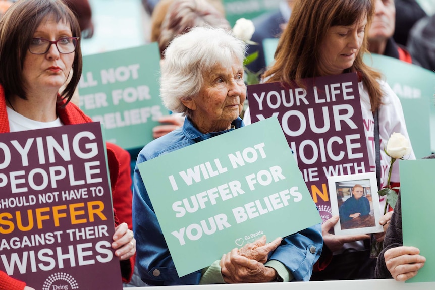 Three women holding voluntary euthanasia signs at a rally at WA Parliament House.