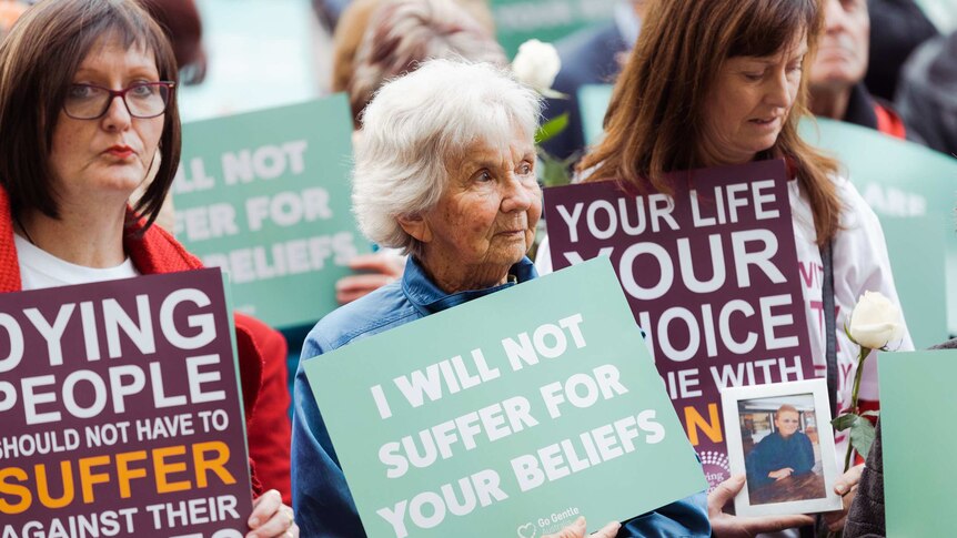 Three women holding voluntary euthanasia signs at a rally at WA Parliament House.